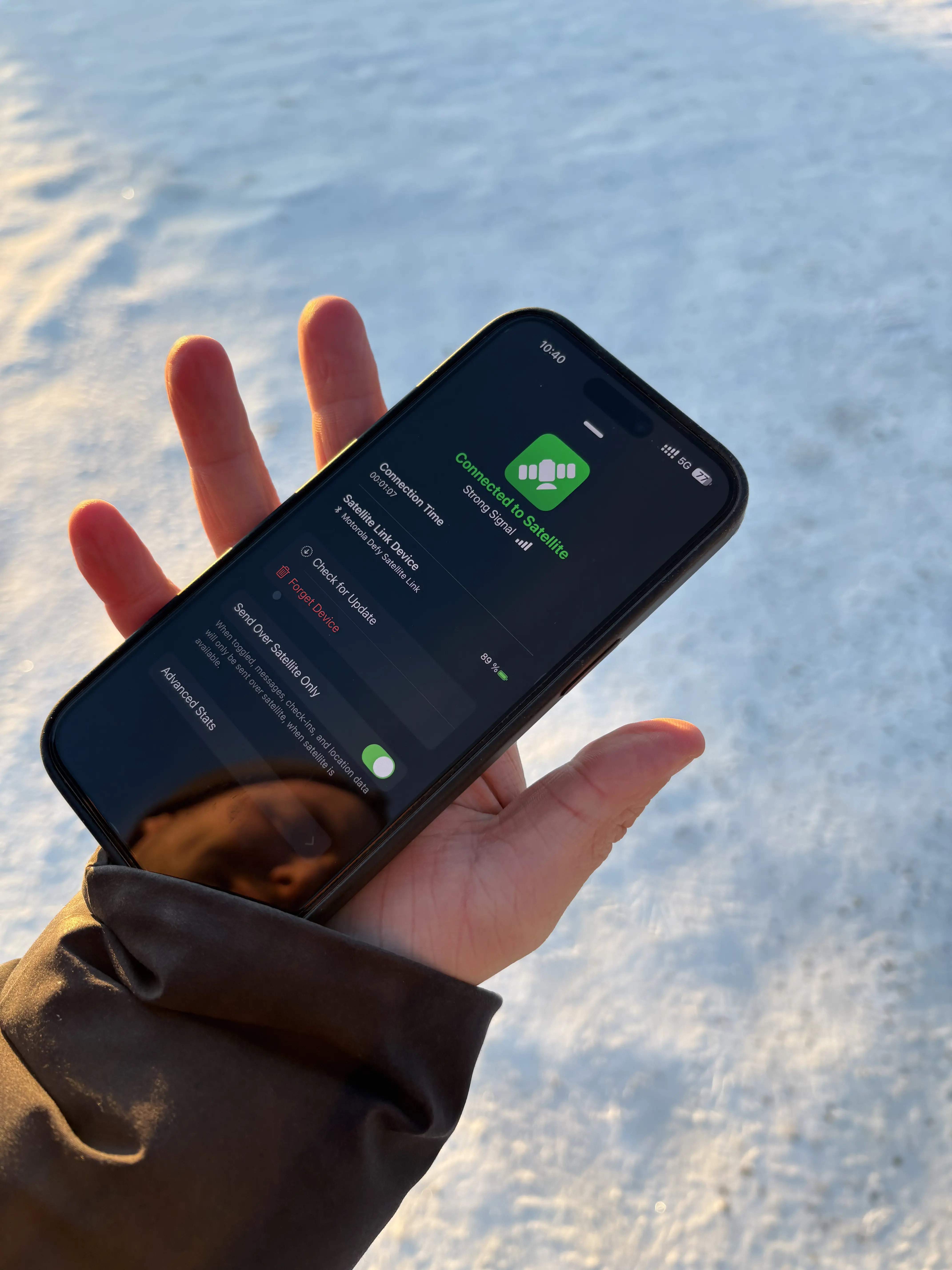 Hand holding a smartphone displaying "Connected to Satellite" and "Strong Signal" on a snowy background, confirming successful Arctic connectivity.